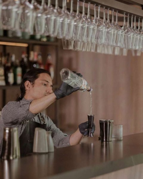 Bartender profesional preparando cóctel en Etro Rooftop Medellín con barra elegante, botellas premium y cristalería suspendida