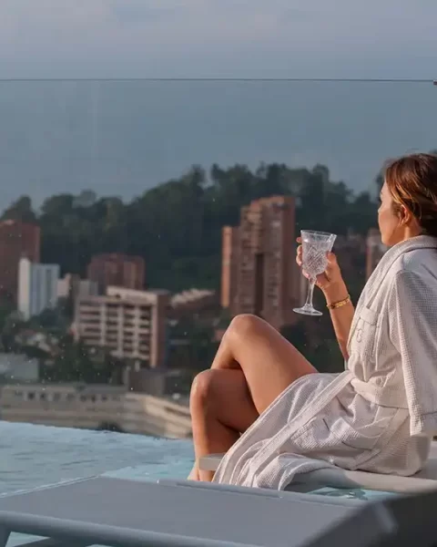 Mujer en bata BINN con copa junto a piscina infinita y vista al skyline de Medellín, experiencia Día de las Madres.