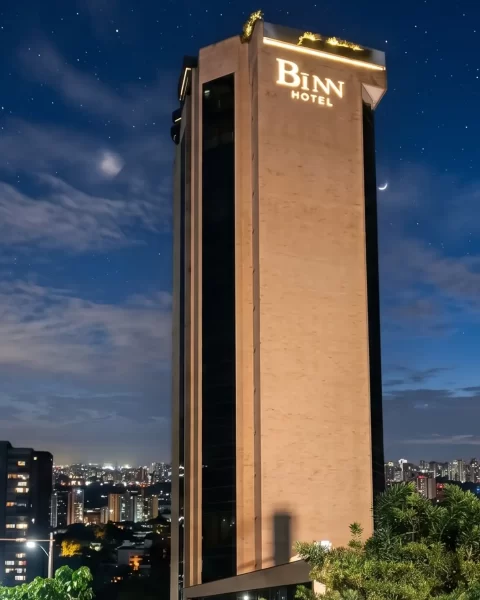 Torre de BINN Hotel iluminada de noche con el skyline de Medellin y cielo estrellado de fondo.
