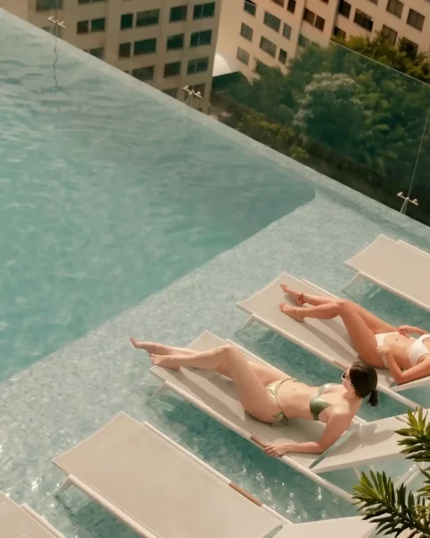 Dos personas tomando sol en sillas al borde de la piscina infinity del rooftop de BINN Hotel