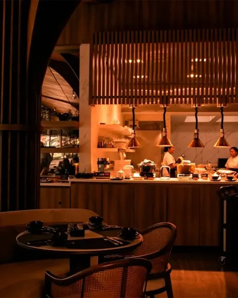 Salón para cena de grupo en La Makha con vista a la cocina abierta, iluminación cálida y mesas preparadas.