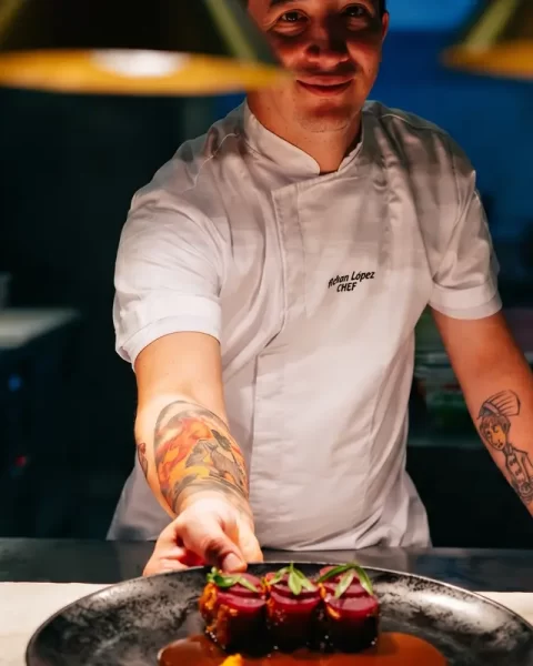 Chef del restaurante La Makha en Medellín presentando un plato de autor sobre la barra de cocina.