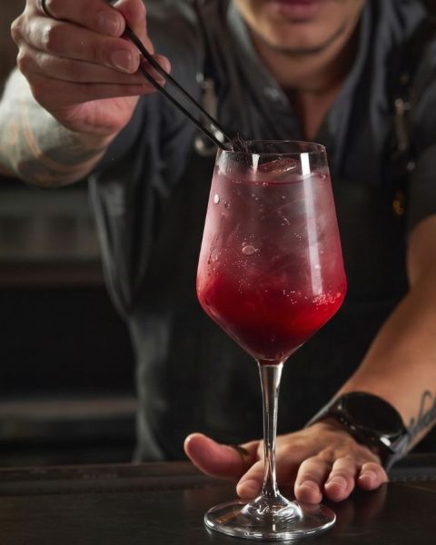 Bartender decorando un cóctel artesanal rojo en copa de cristal, reflejando la coctelería de lujo en Medellín.