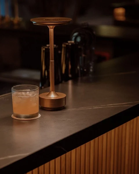 Vaso de cóctel artesanal servido junto a una lámpara dorada en la barra de Etro Rooftop para la temporada de lluvias.