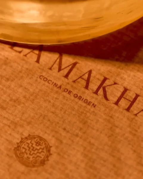 Detalle del logo y menú de cocina de origen para el desayuno en La Makha Medellín sobre un mantel individual con iluminación cálida.