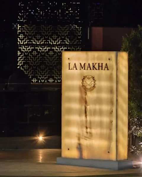 Entrada al restaurante La Makha en Medellín: tótem de mármol retroiluminado con logo dorado en un ambiente nocturno elegante.