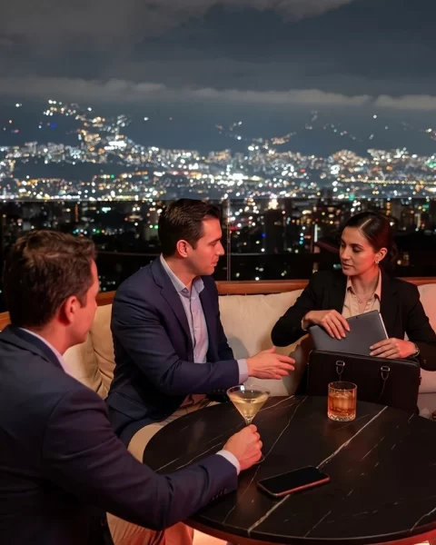 Tres profesionales en reunión afterwork en Etro Rooftop de Binn Hotel con skyline nocturno de Medellín.