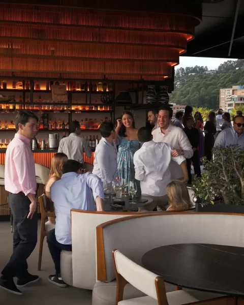 Grupo conversando en Etro Rooftop de Binn Hotel con barra iluminada y vegetación de El Poblado al fondo