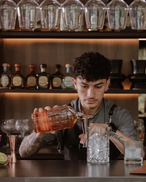 Bartender de Etro Rooftop en Binn Hotel vertiendo bourbon sobre hielo en la barra en Medellín.