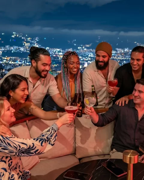 Grupo brindando con cócteles en ETRO Rooftop de BINN Hotel con vista nocturna a Medellín en puente de mayo.