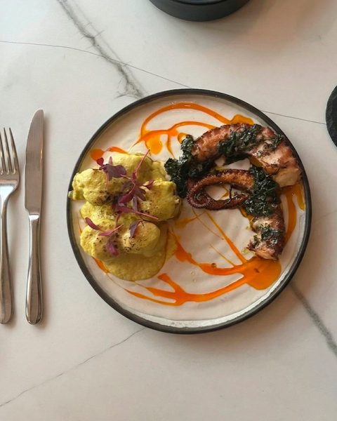 Plato de cocina fusión mediterránea y colombiana en La Makha Medellín: Pulpo grillado con papas criollas en salsa de cúrcuma sobre mesa de mármol.