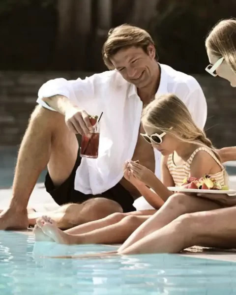 Vacaciones en Binn Hotel de lujo familiar en Medellín: padres e hija relajándose con snacks en zona de piscina premium.
