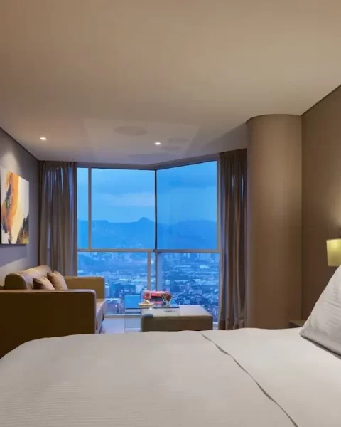 Junior Suite Deluxe room at Binn Hotel Medellin featuring a luxury bed, seating area with sofa, and floor-to-ceiling windows with city views