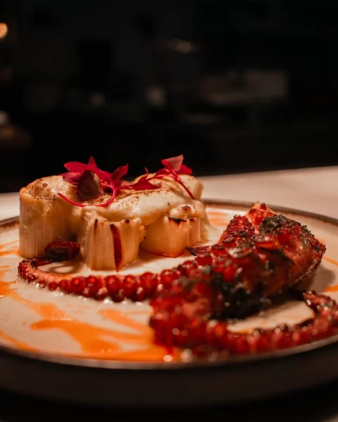 Pulpo a la brasa con salsa naranja y flores rojas en restaurante La Makha de BINN Hotel