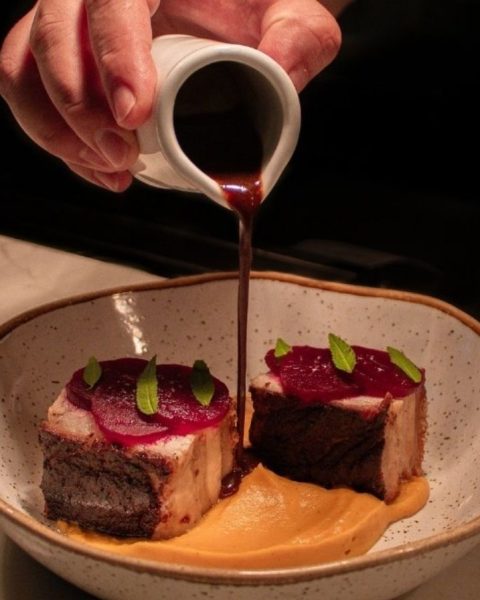 Persona vertiendo salsa sobre un plato de carne, destacando la narrativa visual de la makha