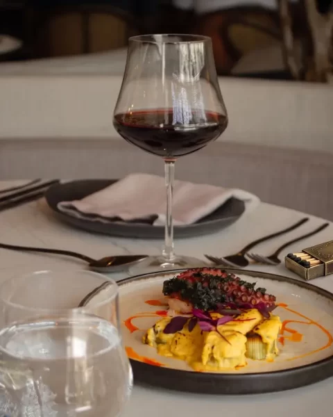 Plato gourmet de pulpo a la parrilla sobre salsa amarilla servido junto a una copa de vino tinto en una mesa de mármol del restaurante La Makha en Medellín.