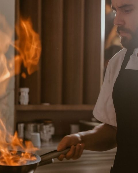 Hombre con delantal de chef cocinando en la estufa, preparando platos perfectos para compartir en Etro