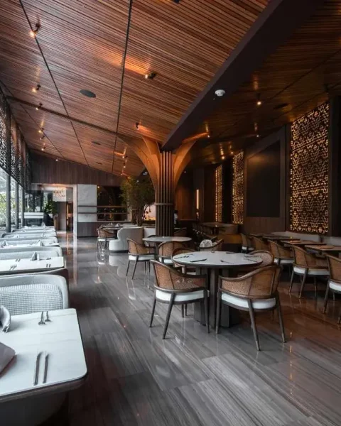 Salón interior del restaurante La Makha en Medellín con mesas dispuestas, sillas de madera y diseño arquitectónico moderno.