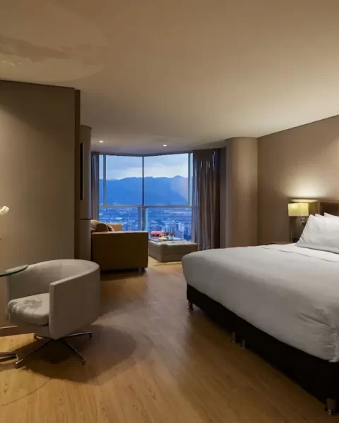 Superior King Room at Binn Hotel Medellin featuring a king-size bed, glass table with two chairs, and floor-to-ceiling windows with city views