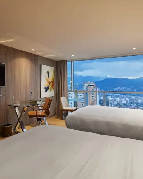 Superior Twin Room at Binn Hotel Medellin featuring two twin beds, a work desk, flat-screen TV, and floor-to-ceiling windows with city views