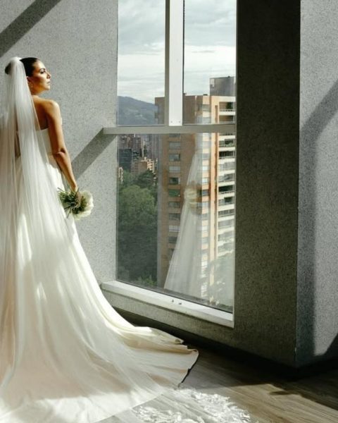 A bride stands by a window, gazing at a stunning city view, showcasing the ideal hotel for your wedding