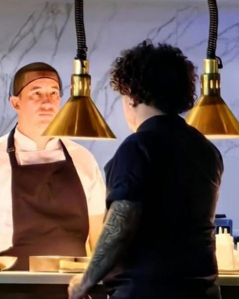 Dos chefs, David Suárez Estrada y su compañero, están de pie en un mostrador de restaurante, listos para cocinar