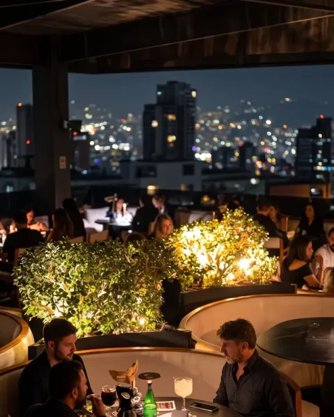 Terraza iluminada de noche llena de clientes disfrutando de la vista nocturna de la ciudad en Etro Rooftop Medellín.