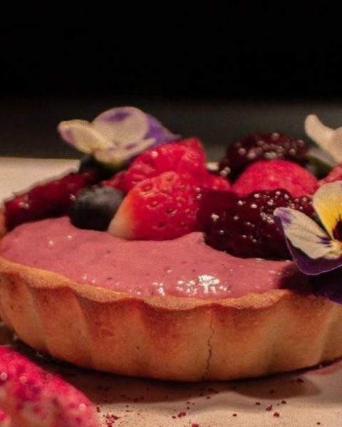 Postre decorado con frutas del bosque y flores, servido en un plato. Vive la experiencia completa de La Makha.