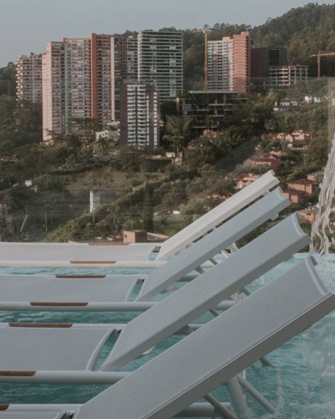 Lounge chairs by a pool offer a serene view of the city skyline, perfect for relaxation and wellness